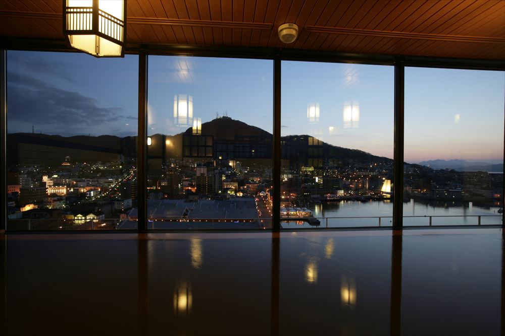 LA VISTA Hakodate Bay_Indoor bath of the large common bathing area. Immerse yourself in the beautiful silhouette of Mt. Hakodate against the setting sun seen through the large windows.