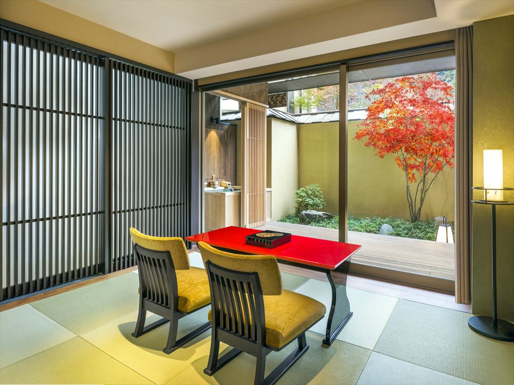 스이란 럭셔리 컬렉션 호텔 교토. '유즈노하' 디럭스 트윈 킹에서는 주홍색 테이블과 황금색 의자가 객실을 장식합니다.